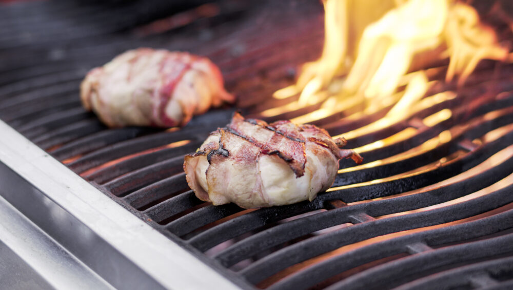 detail sýru obaleném ve slanině na grillu, v pozadí šlehá plamen z grillu