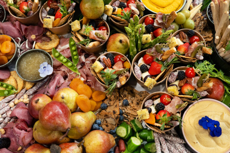 Plný stůl zblízka – uzeniny, sýry, čerstvé ovoce a fingerfood kelímky